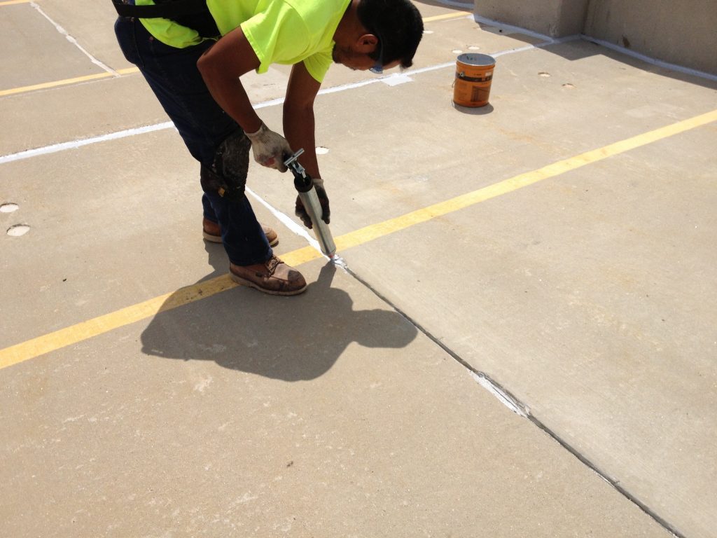 A worker replacing sealant at a garage's top deck.