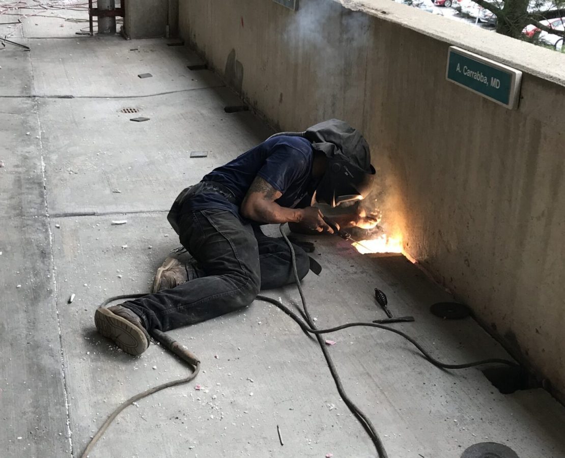 A welder repairs a broken connection in a parking structure.