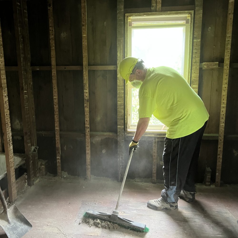 A man sweeps a floor while wearing a dust mask